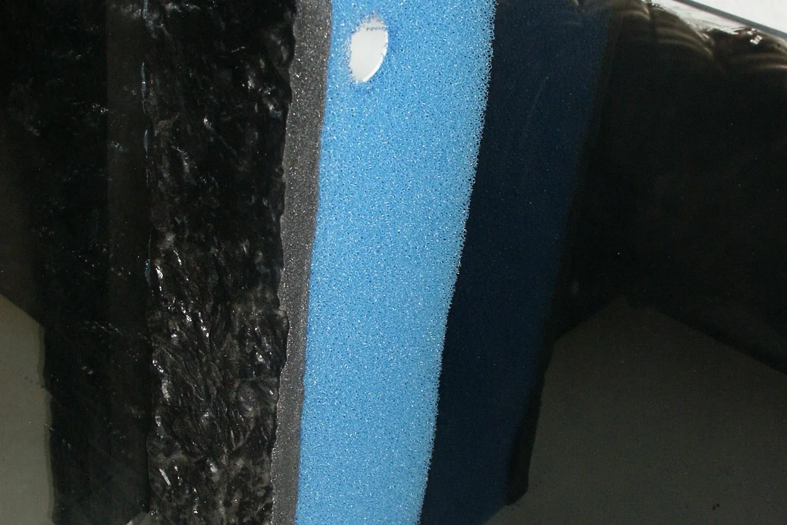 A black and blue foam filter mat fitted across the corner of an aquarium